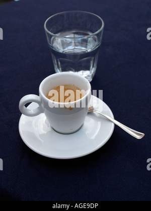 leere Espresso Tasse und Untertasse und Glas Wasser am Tisch mit blauen Tischdecken Stockfoto