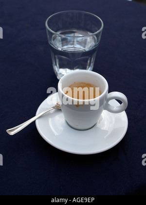 leere Espresso Tasse und Untertasse und Glas Wasser am Tisch mit blauen Tischdecken Stockfoto