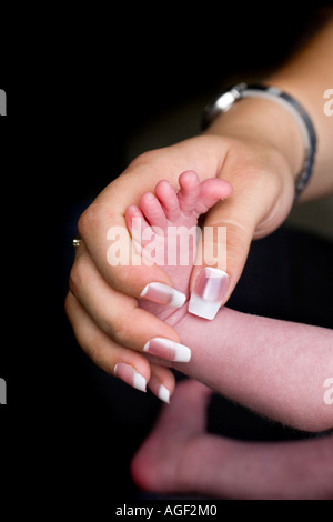 EIN ZWEI WOCHEN ALTES WEIBLICHES BABY FUß UND BEINE MIT MÜTTER HANDHOLDING Stockfoto