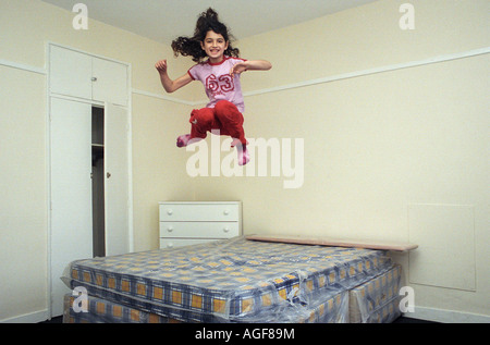 Ein junges Mädchen, im Alter von 9, springt auf ein Bett in einem leeren Zimmer. Stockfoto
