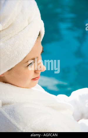 Kaukasischen Mitte Erwachsene Frau mit Bademantel und Handtuch auf Kopf sitzen neben pool Stockfoto