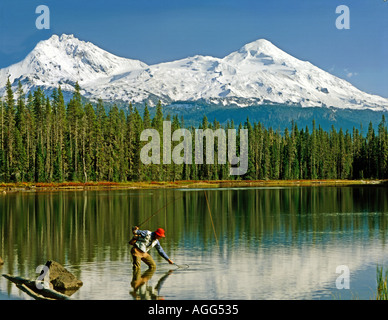 Scott See Fischer netting eine Forelle unter den wachsamen Augen der verschneiten Norden und Mitte Schwester Bergen in Oregon Stockfoto