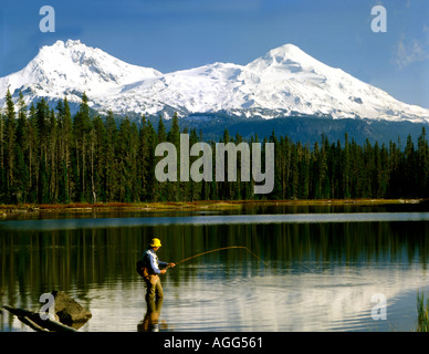 Scott See Fischer netting eine Forelle unter den wachsamen Augen der verschneiten Norden und Mitte Schwester Bergen in Oregon Stockfoto