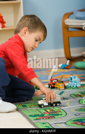 drei Jahre alte Junge spielt mit Spielzeug-LKW auf Matte mit Straßen und Häusern drauf Stockfoto