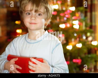 fröhlicher Junge am Weihnachtsmorgen grinsend hielt eine große roten vorhanden Stockfoto