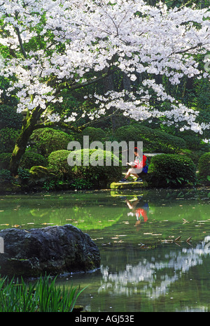 Japanische Mädchen sitzt neben einem Buch unter Kirschblüten in Kyoto Park im Frühjahr Teich Stockfoto