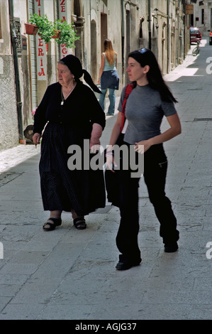 Eine alte Frau traditionell in schwarz gekleidet mit jungen Frauen in moderner Kleidung in Scanno in der Region Abruzzen in Italien Stockfoto