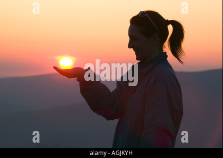 Eine Frau mit der untergehenden Sonne in der Seenplatte, Cumbria, UK Stockfoto
