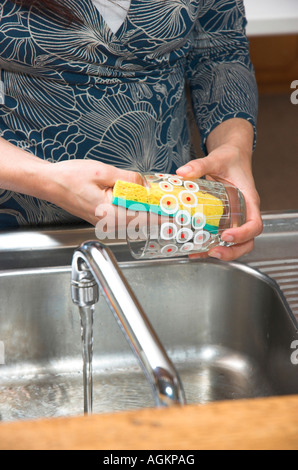 Frau ein Glas bei der Küchenspüle waschen, während Wasser aus dem Hahn läuft Stockfoto