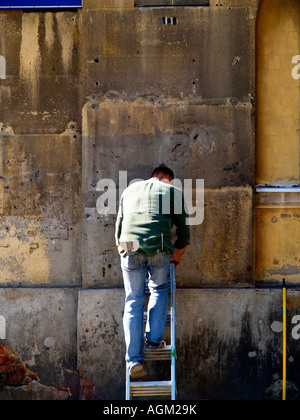 Auftragnehmer oder Bau Arbeiter auf einer Leiter arbeitet zu reparieren oder wieder auftauchen, eine alte outdoor-Wand in Krakau, Polen. Stockfoto