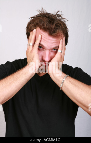 Müde und erschöpft attraktive junge 20er Jahre männlichen Mann hält Kopf in Händen, die verschlafenen Blick gelangweilt erschöpft ausgebrannt über gearbeitet Stockfoto