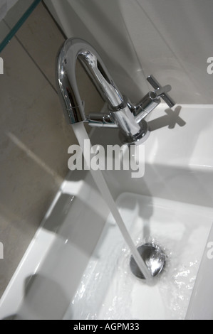 WASSER AUS DEM WASSERHAHN FLIEßT NACH UNTEN OFFENEN ABFLUSS DES WEIßEN WASCHBECKEN Stockfoto