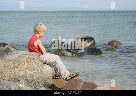 Junge sitzt auf den Felsen in reflektierende Stimmung Armen gefaltet in Skagen Jütland Dänemark Stockfoto