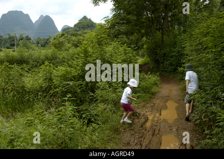 China Guangxi Yangshuo zwei junge europäische Kinder zu Fuß auf A schlammigen Feldweg entlang der Reisfelder Stockfoto