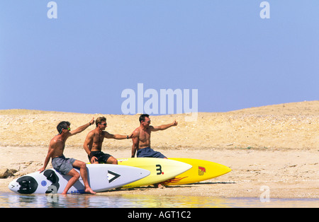 Drei männliche Windsurfer in Shorts mit ihren Surfbrettern versuchen hitching eine Fahrt oder einen Aufzug am Roten Meer Sandstrand Sinai Ägypten Stockfoto