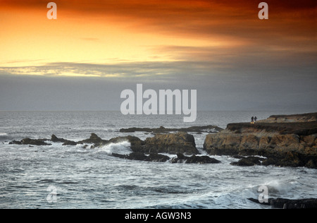 Sonnenuntergang und zwei Personen und ihre Fahrräder entlang einer zerklüfteten Küste am Montana de Oro State Park in der kalifornischen Zentralküste. Stockfoto