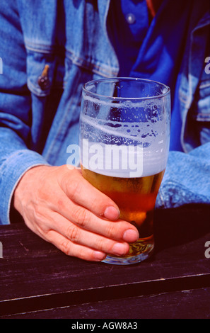 EIN MANN HÄLT EIN HALB BETRUNKEN PINT BIER IN SEINER RECHTEN HAND NAHAUFNAHME Stockfoto