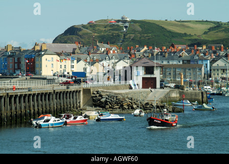 Hügelige Landschaft mit Blick auf das Stadtzentrum von Aberystwyth und den Hafen Mit rotem Fischerboot Putting to Sea Ceredigion Wales UK Stockfoto