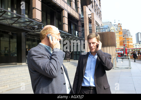 Zwei Männer in Anzügen, die Arbeiten in der Stadt in Finance-Geschäft nutzen Handys plaudern und tratschen in der Nähe von Liverpool Street Stockfoto