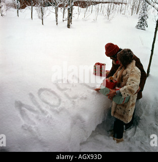 Weihnachtsszene mit jungen Paar beladen mit Geschenken anhalten, um das Wort NOEL in einem Snowbank schreiben Stockfoto