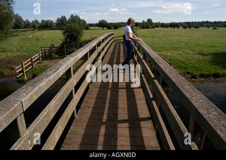 Eine Frau mittleren Alters auf eine hölzerne Brücke über den Fluss Stour am historischen Flatford in Suffolk England Stockfoto