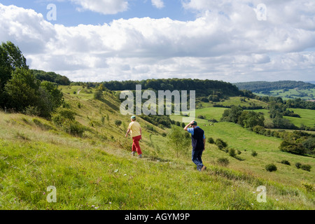 Ein Paar, das an einem windigen Tag auf dem Cotswold Scarp in Barrow Wake in der Nähe von Birdlip, Gloucestershire, Großbritannien, den Cotswold Way entlang geht Stockfoto