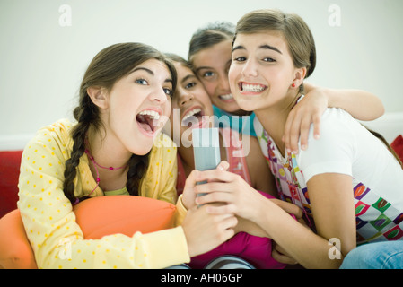 Junge weibliche Freunde sitzen zusammen, singen in Fernbedienung Stockfoto