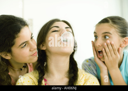 Drei jungen Freundinnen, eine Sprengung Blase, während andere zusehen Stockfoto