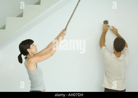 Frau malt man Decke mit Walze Erweiterung, wechselnden Glühbirne Stockfoto