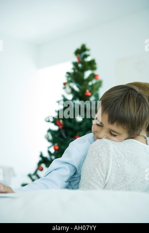 Mutter saß auf Sofa, halten jungen in Armen, Weihnachtsbaum im Hintergrund, junge, Lächeln Stockfoto