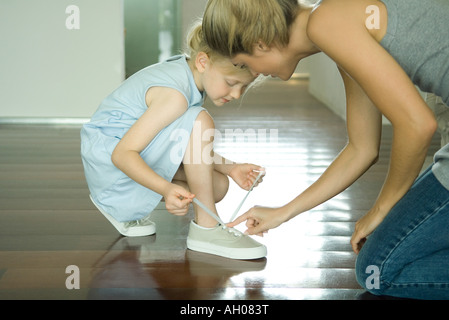 Mutter hilft wenig Mädchen, die Schnürsenkel zu binden Stockfoto