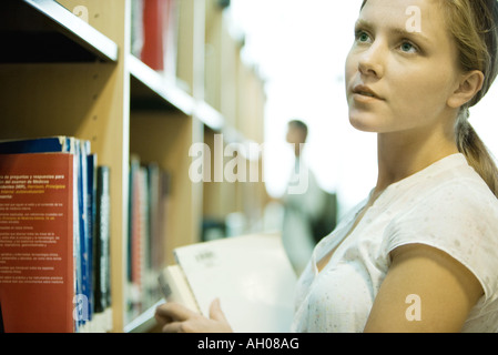 Junge Frau betrachten Regalen der Bücher in der Bibliothek Stockfoto