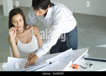 Paar auf der Suche auf Blaupausen zusammen, Mann über Frau Schulter, unter Hinweis auf die Blaupause Stockfoto