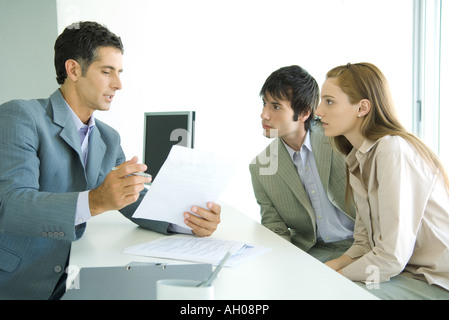 Junges Paar sitzt auf Schreibtisch von Geschäftsmann, Unternehmer erklären, Dokument Stockfoto