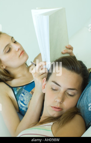 Junge Frau Lesebuch, Freund Kopf auf ihren Schoß ruht, mit geschlossenen Augen, geneigt Ansicht Stockfoto