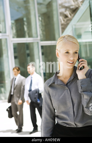 Junge Geschäftsfrau mit Handy im Freien, wegsehen, Geschäftsleute, die im Hintergrund laufen Stockfoto