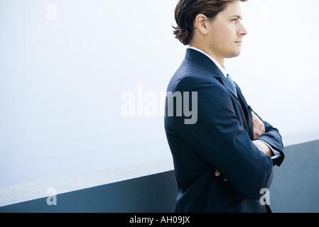 Junger Geschäftsmann stehend mit Armen gefaltet, beschnitten, Seitenansicht Stockfoto