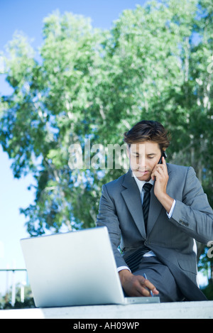 Junge Unternehmer sitzen im Freien mit Handy und Laptop-Computer, schreiben Stockfoto