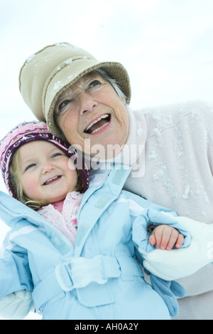 Ältere Frau umarmen Enkelin im Schnee, beide Lächeln, Taille bis Stockfoto