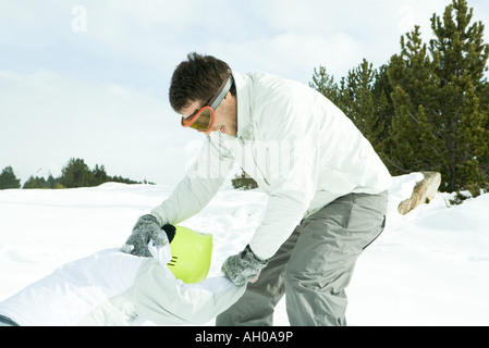 Zwei junge Freunde spielen im Schnee, eine die andere nach oben ziehen Stockfoto