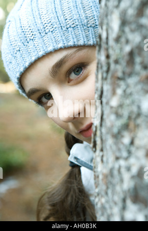 Teenager-Mädchen spähen um Baumstamm, Blick in die Kamera, Porträt Stockfoto