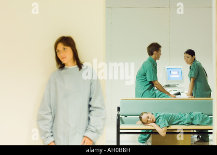 Angehörigen des medizinischen Personals im Chat im Büro, eine liegend auf Bank, weibliche Patienten stehen im Vordergrund Stockfoto