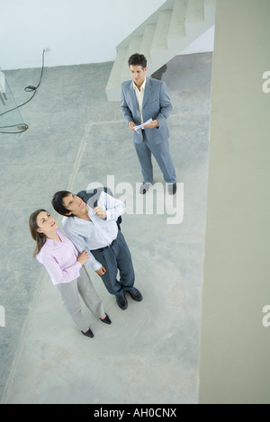 Männliche Immobilienmakler in Wohngebäude mit voller Länge, junges Paar, erhöhte Ansicht stehen Stockfoto