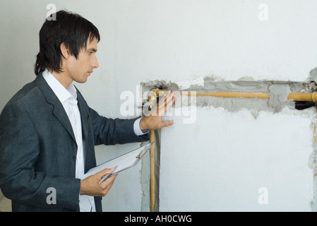Mann im Anzug, die Inspektion von Rohren in Wand Stockfoto