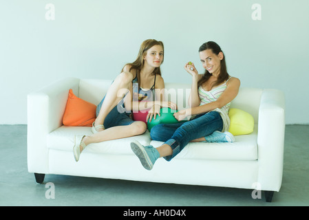 Zwei junge Freunde auf Couch sitzen, Lächeln in die Kamera, in voller Länge Stockfoto