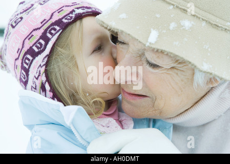 Kleinkind Mädchen küssen Großmutter auf Wange, beide gekleidet in Winterkleidung, Nahaufnahme Stockfoto