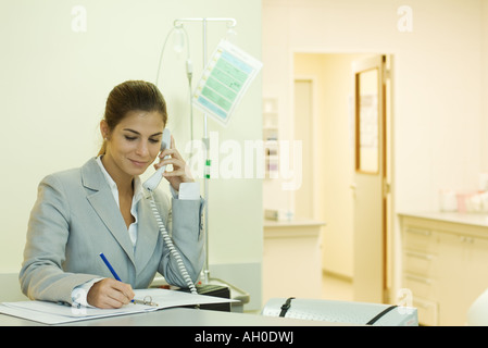 Junge Frau in Arztpraxis, mit Telefon, schriftlich Stockfoto