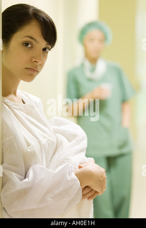 Junge Frau mit Neugeborenen, Blick in die Kamera, medizinische Arbeiter im Hintergrund Stockfoto