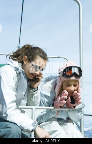 Junge Freunde am Sessellift, eine mit Handy, beide in Winterkleidung gekleidet Stockfoto