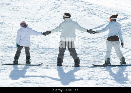 Drei junge Snowboarder stehen zusammen, Rückansicht Hand in Hand, Stockfoto